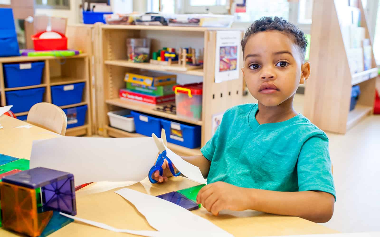 Educare boy at table with scissors and paper