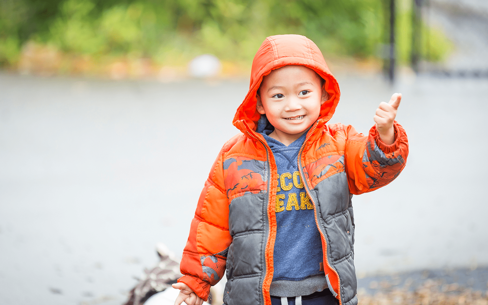 Little boy standing outside in orange raincoat