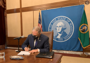 Gov Inslee signing bill alone with the caption “Missing the people and the smiles…”
