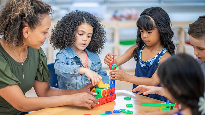 Teacher sitting at table with students while their doing an activity in the classroom