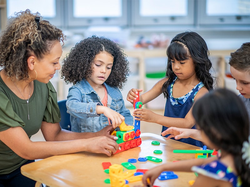 Teacher sitting at table with students while their doing an activity in the classroom