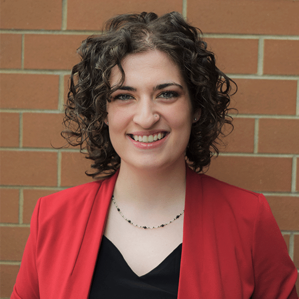 Naomi Black wears a red jacket standing in front of a brick wall