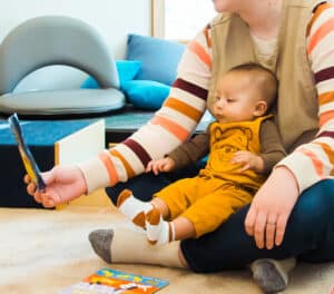 Caregiver holding book in front of a small infant's face and reading.