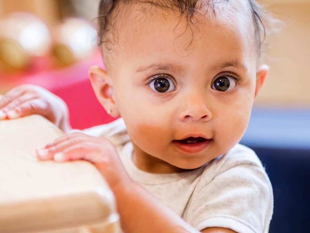 Young child holding herself up against table