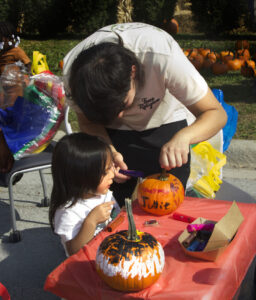 Caregiver painting pumpkin with child looking and painting too