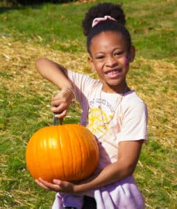 Little girl holding pumpkin in front of a field