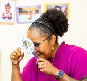Teacher with purple shirt holding printed handheld sign like a spyglass