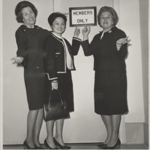 Black and white photo of U.S. Rep. Charlotte Reid (R-Virginia), Rep. Patsy Mink (D-Hawai’i), Rep. Catherine May (R-Washington) in front of a "Members Only" sign where Rep. Reid and Rep. May are shrugging and Rep. Mink and Rep. May are pointing to the "Members Only" sign.