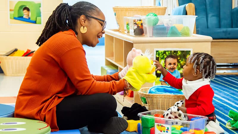 Teacher using puppet to play with infant on floor