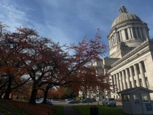 Photo of the Washington State Capitol Building in Olympia, Washington taken from the side on a sunny Fall day with red and green fall leaves on the trees in front of the building.