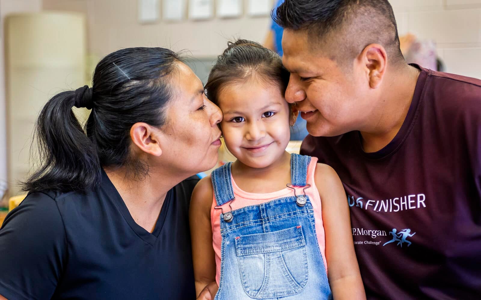 Mother and father kissing child on the cheek.