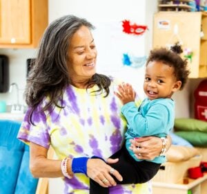 Woman in tie-dye holding child and smiling.