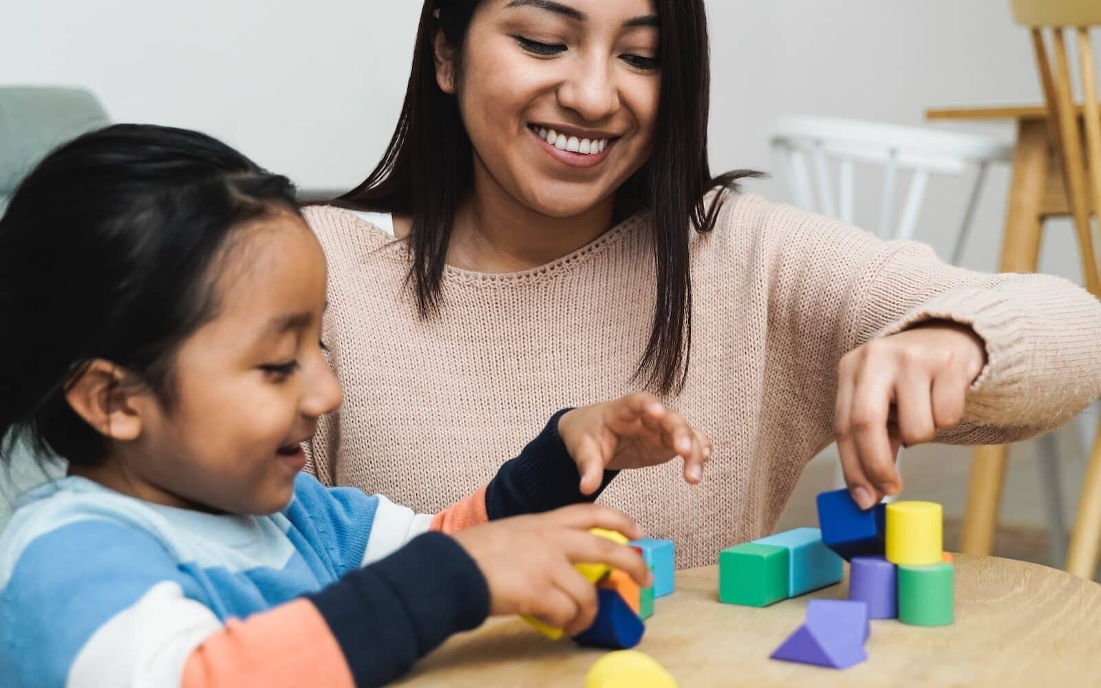 Latin American mother and son child having fun playing games with wood toy bricks at home - Family time together