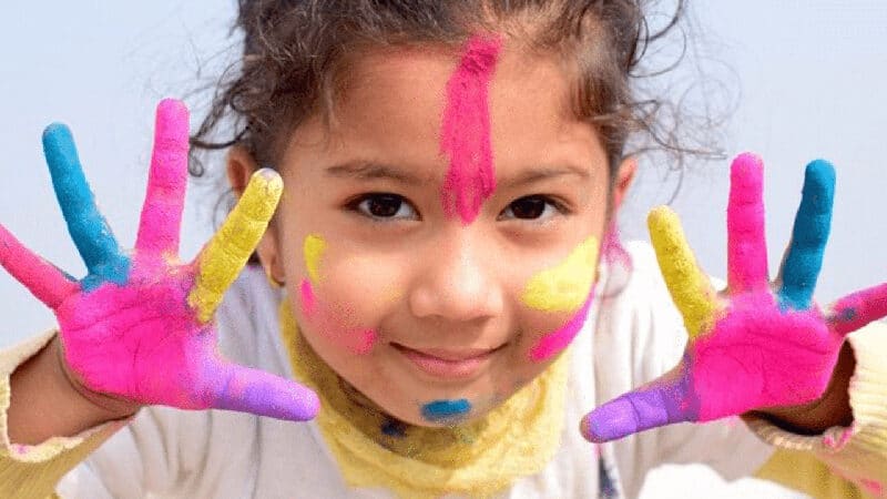 Little girl smiling at camera with painted hands.