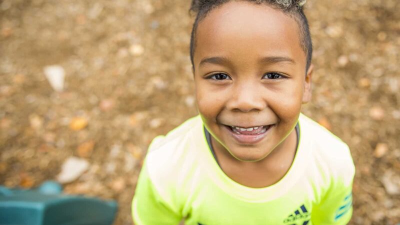 Little boy smiling and standing in front of leaves in the background